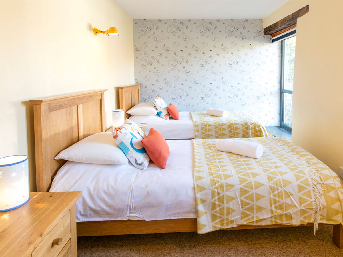 A bright sunny twin bedroom with a blue framed window and two single beds with yellow bedspreads