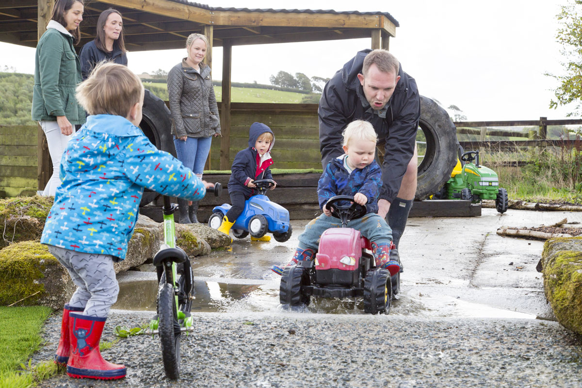 Young boy on a kids ride on tractor being pushed by man around the Balance Bike Track at Tredethick