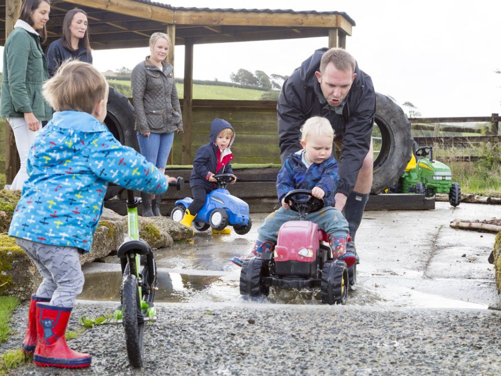 Young boy on a kids ride on tractor being pushed by man around the Balance Bike Track at Tredethick