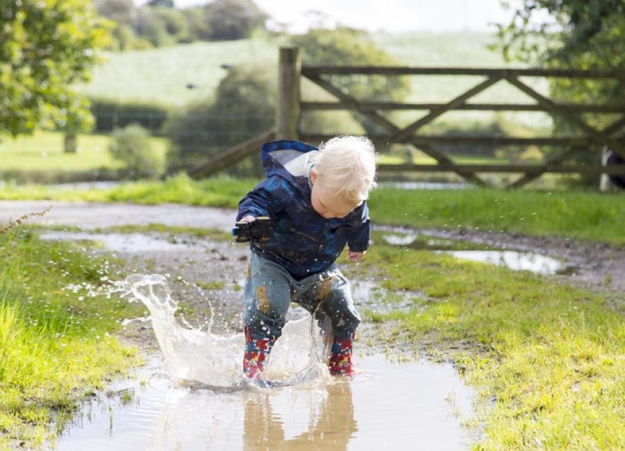 Young boy splashing in a puddle with wellies