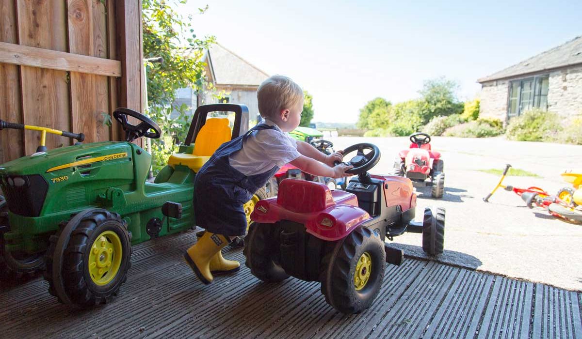 Toddler getting started on a toy tractor and playing in the sunshine