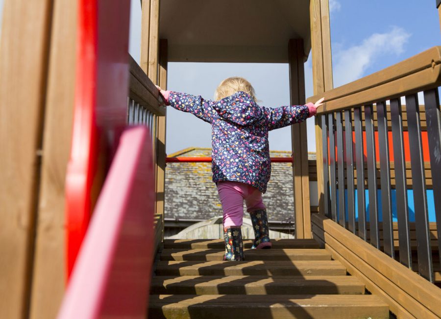 Small child climbing up steps on a play park frame