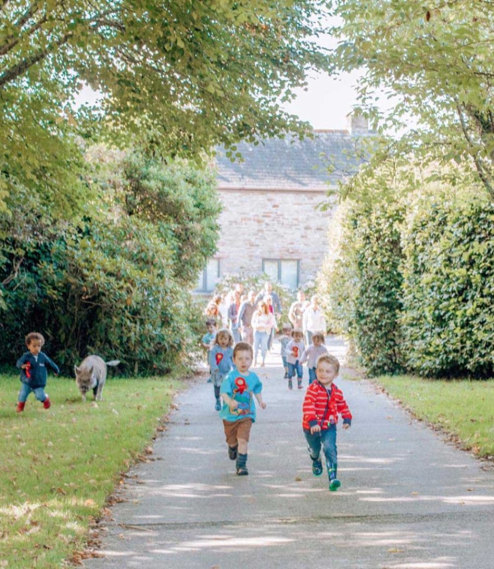 Children running around the gardens with a pig at Tredethick in Cornwall, UK