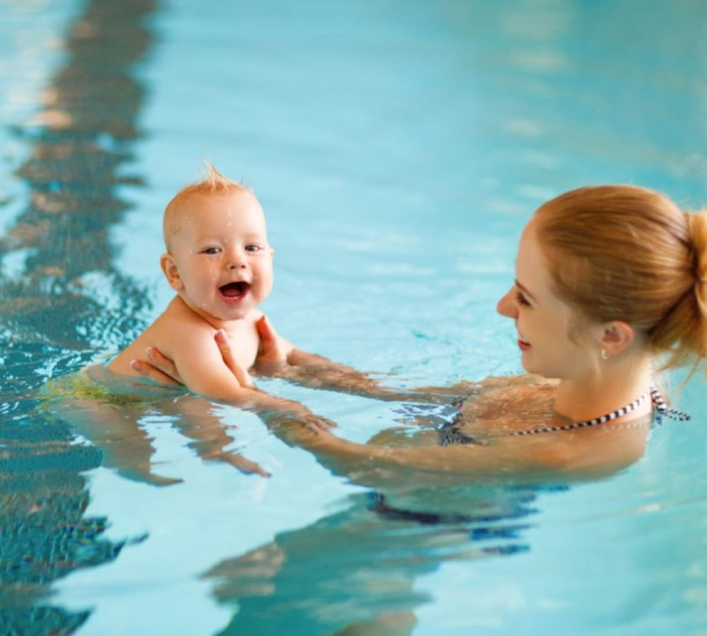 A woman holding a smiling baby in a swimming pool.