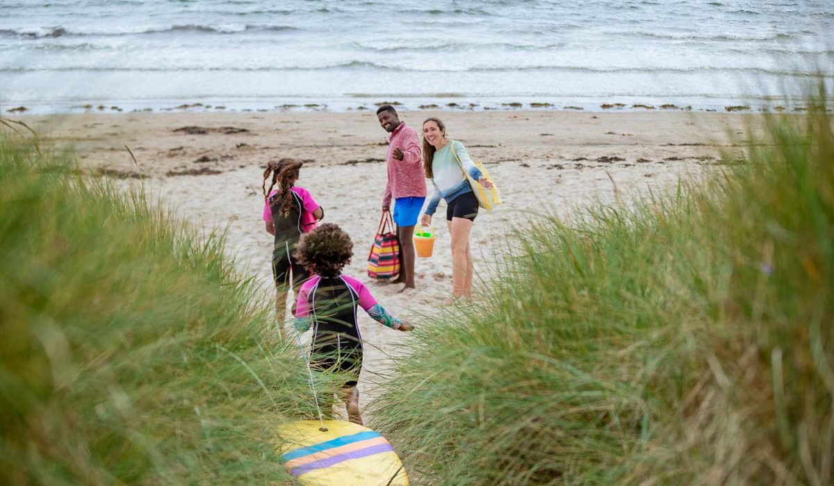 Young family in wetsuits running down to the sea with a body board