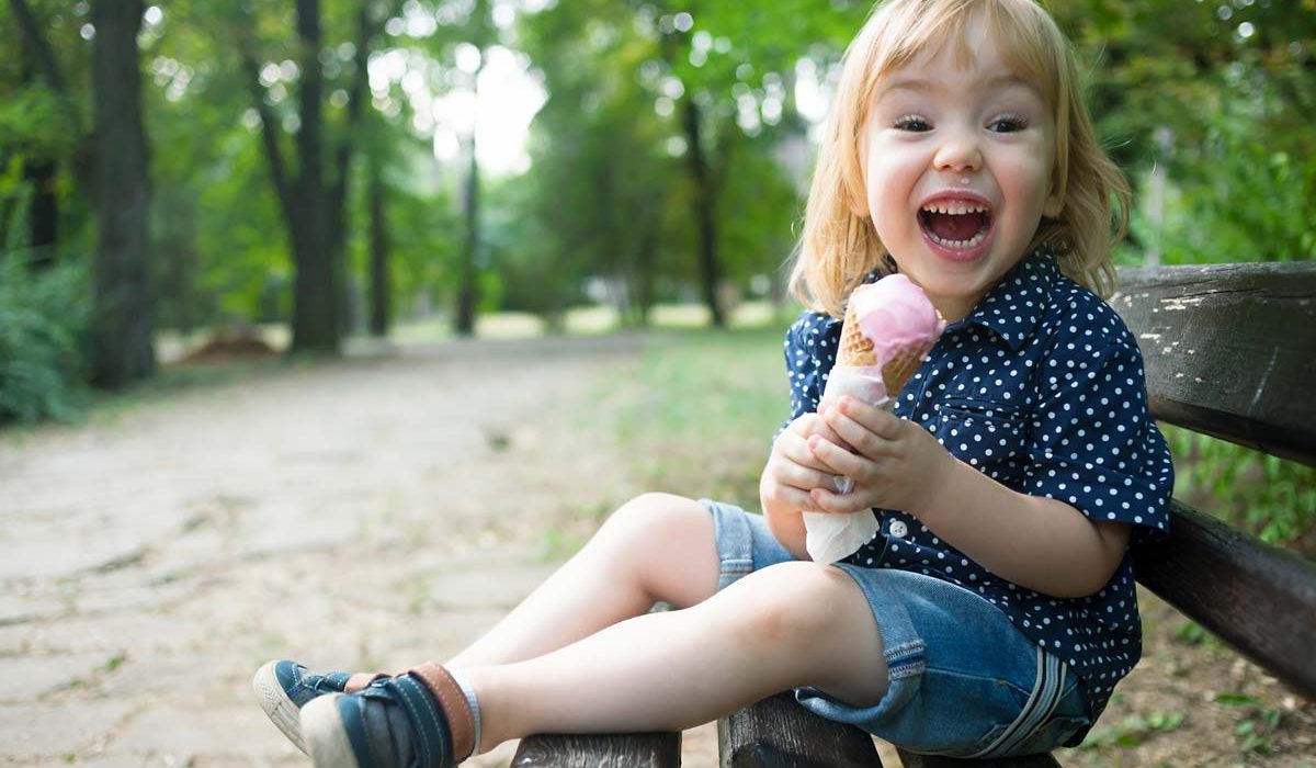 Little blond boy eating ice cream in a cone and having fun in a park.