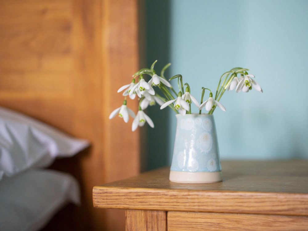 Snowdrops in a blue vase on a wooden bedside table