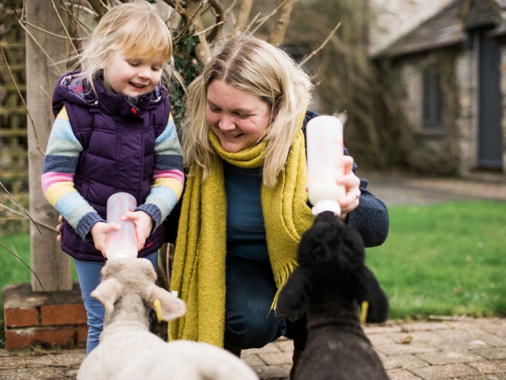 Woman and young girl bottle feeding a baby lamb at Tredethick