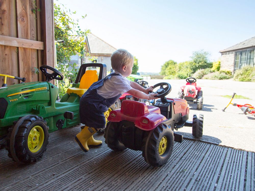 A toddler in yellow wellies pushes along a red ride along tractor