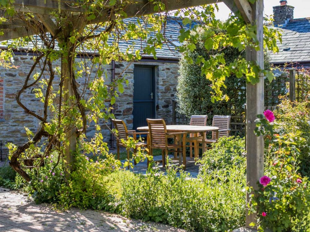 Garden at Tredethick Farm Cottages in Cornwall. There are plants and wooden garden furniture.