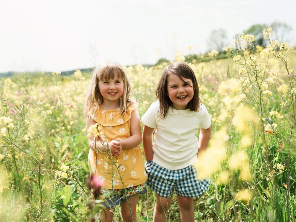 Two young girls smiling in a field at summer time