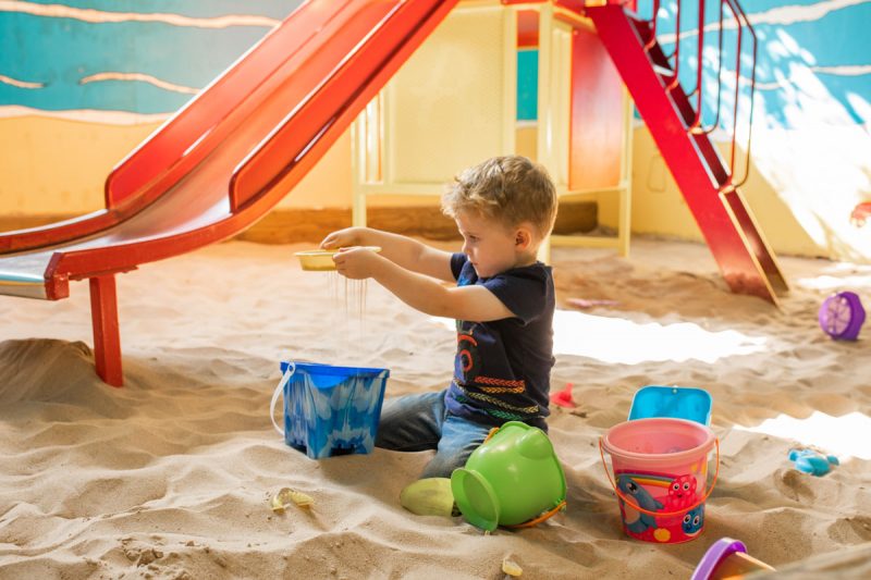Young boy playing with sand, surrounded by buckets in the indoor play barn