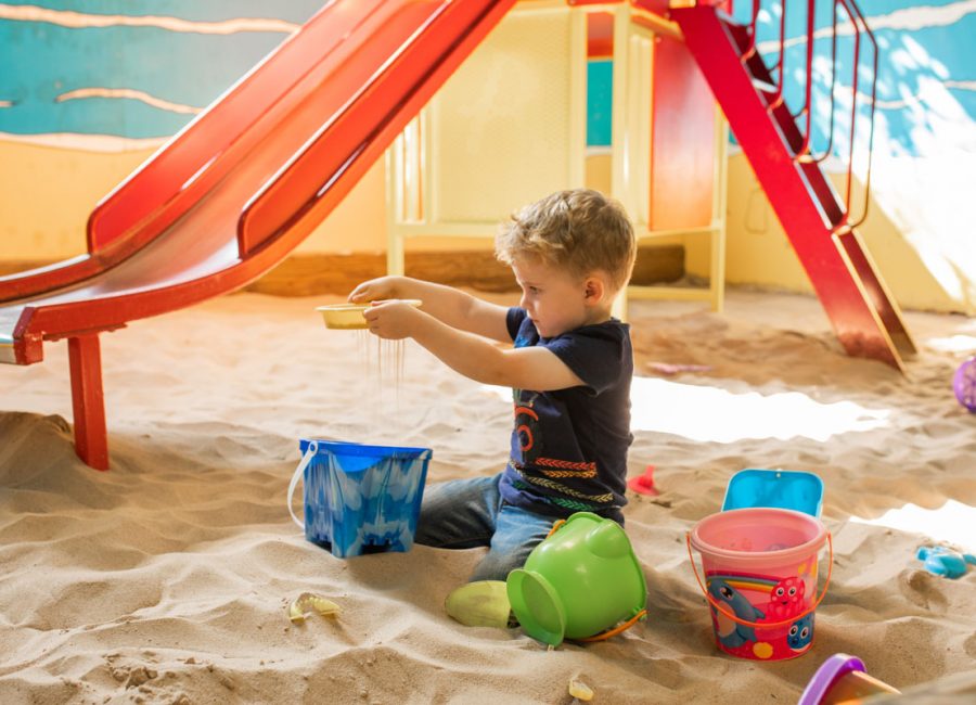 Young boy playing with sand, surrounded by buckets in the indoor play barn