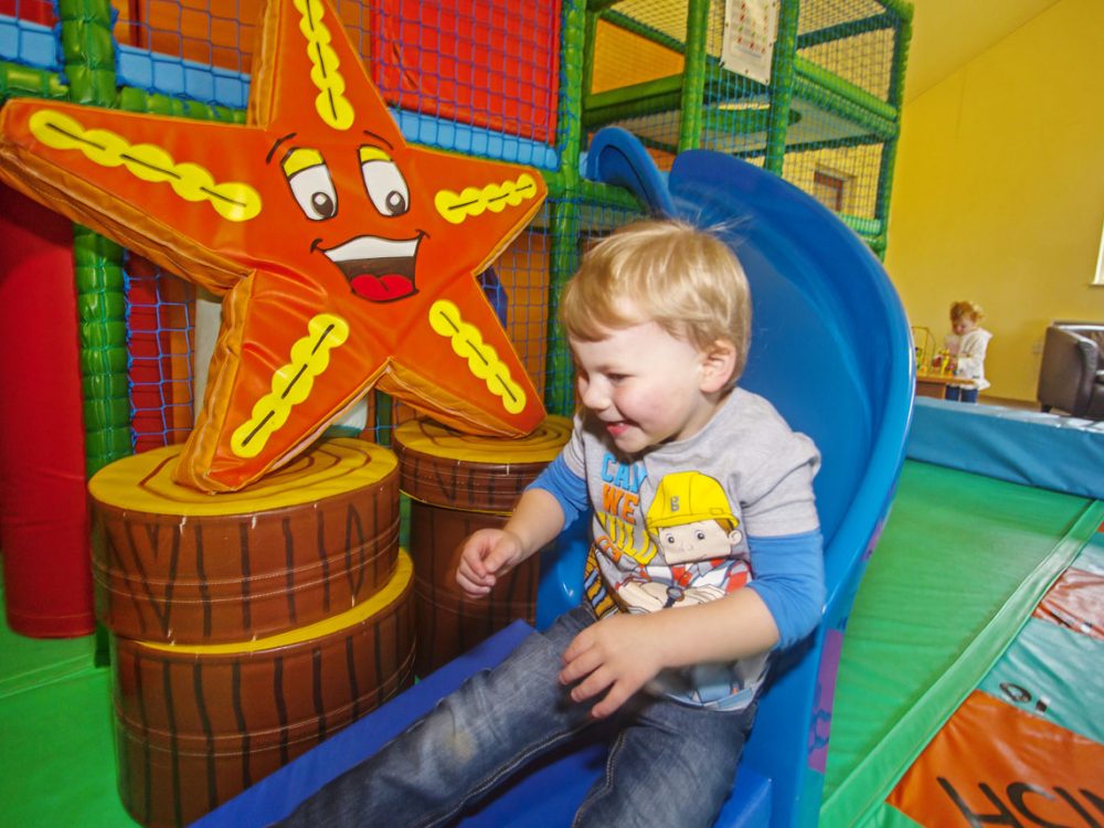 Smiling young boy riding down a slide in the soft play area