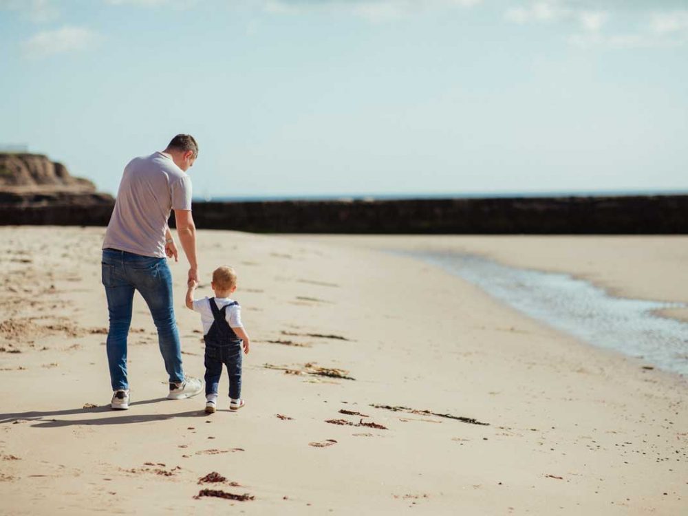 Father and son walking along a beach during a toddler break in Cornwall.