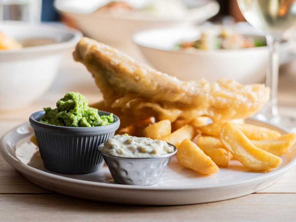 Fish and chips with mushy peas and tartar sauces served with a glass of white wine.