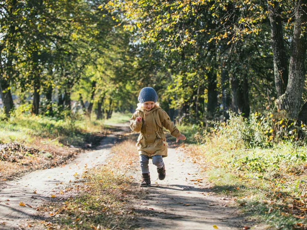 Little girl running along a trail path. She's wearing warm clothing.