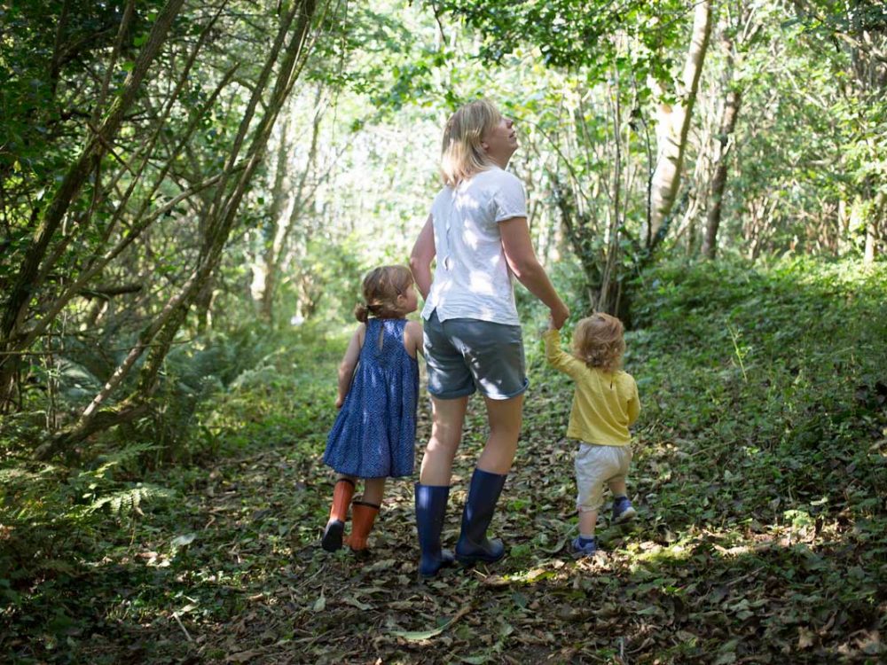 A woman walking with two young children through a wooded trail in Cornwall, UK